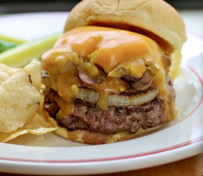 A cheeseburger with potato chips and pickles on a plate